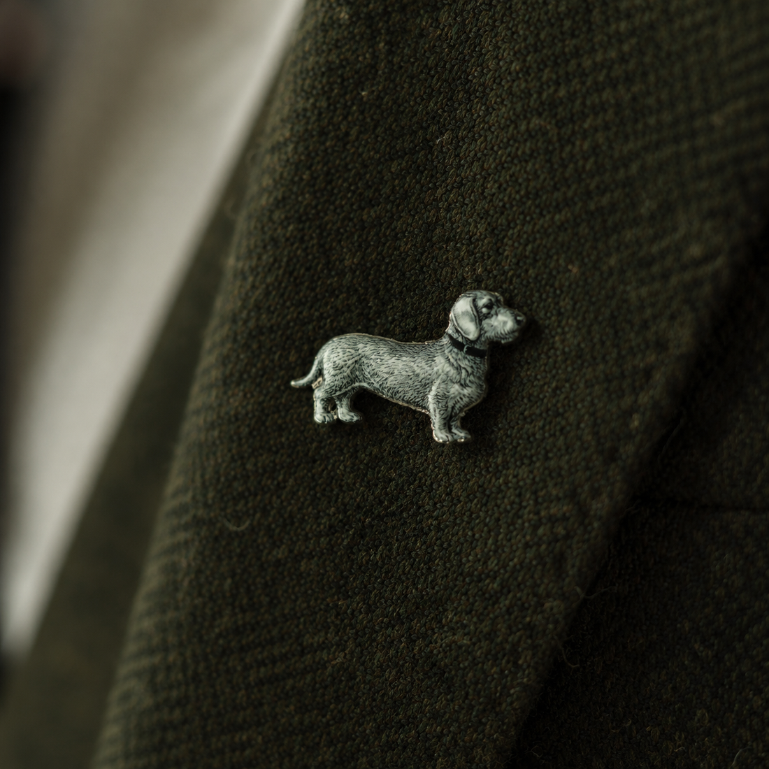 Pin Wilhelm – Rauhaardackel aus Zinn am Revers eines olivgrünen Wollmantels