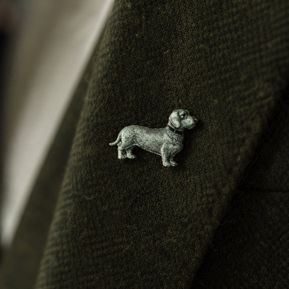Pin Wilhelm – Rauhaardackel aus Zinn am Revers eines olivgrünen Wollmantels